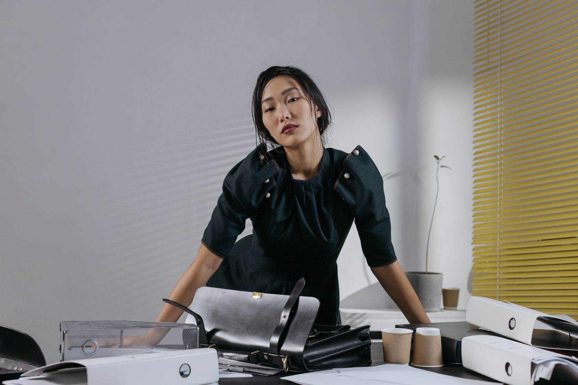 Asian woman in black dress posing confidently in a stylish office setting with modern decor.