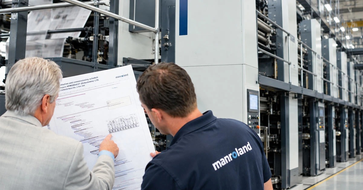 manroland Goss technicians reviewing commissioning schedule next to a large printing press